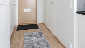 Ein Flur mit einer Holztür, einer schwarzen Matte, einem grauen Teppich mit Muster und weißen Wänden.