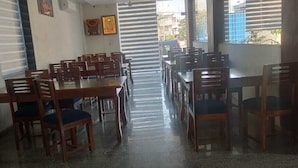 A dining area with multiple wooden tables and chairs, a central aisle, and a view of the outside through large windows.