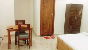 A bedroom with a bed, a wooden wardrobe, a desk with chairs, and a red and white rug.