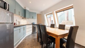 Une cuisine moderne avec des meubles de couleur bleu clair, un réfrigérateur en acier inoxydable et une table à manger en bois avec des chaises noires.