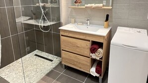 A modern bathroom with a glass-enclosed shower, a vanity with a mirror, and a built-in washing machine. - Apartment "Lune" RDC terrace, private parking (Saint-Julien-Chapteuil)
