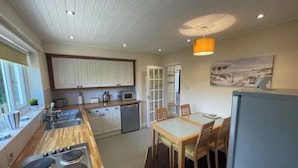 A modern kitchen with a wooden countertop, stainless steel appliances, and a dining area with a table and chairs. - Bungalow with distant sea views (Colwyn Bay)