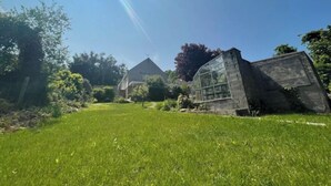 A grassy area with a stone structure and a glass greenhouse. - Bungalow with distant sea views (Colwyn Bay)
