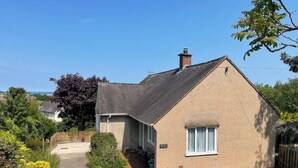 A single-story house with a sloped roof, a chimney, and a small porch with a chair. - Bungalow with distant sea views (Colwyn Bay)
