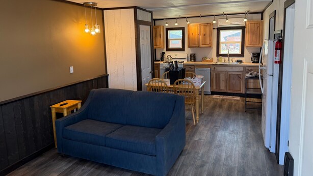 A compact kitchen with wooden cabinets, a dining table, and a blue sofa. - Foothills Lodge 9 Suite - South Fork (South Fork)