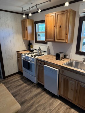 A modern kitchen with wooden cabinets, a gas stove, a dishwasher, and a window providing natural light.