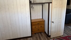 A room with a white wooden wardrobe, a wooden dresser, a door, and a small shelf with a fan. - Foothills Lodge 9 Suite - South Fork (South Fork)
