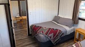 A bedroom with a bed, a wooden chair, a small wooden table, and a door leading to another room. - Foothills Lodge 9 Suite - South Fork (South Fork)