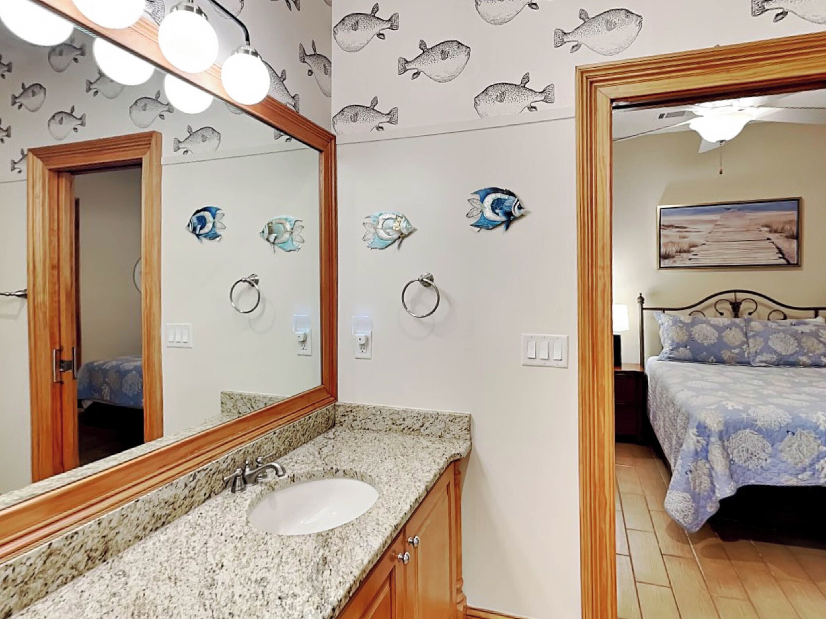 Une salle de bain avec un comptoir en granit, un lavabo et un miroir. On y trouve des porte-serviettes fixés au mur et un luminaire au plafond.