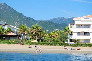 A beachfront property with a pool, palm trees, and a mountain backdrop.