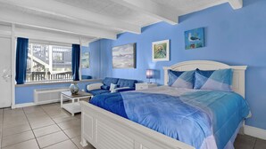A bedroom with a large bed, a nightstand, a window with curtains, and artwork on the walls.