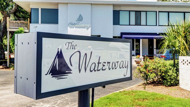 A sign for The Waterway hotel with a modern building in the background.
