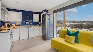 A modern kitchen with white cabinets, a stainless steel refrigerator, and a large window offering a city view. - Luxury Loft Living | Free Parking - Pass the Keys (Brighton)