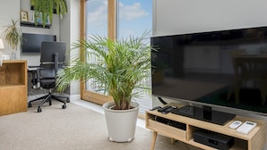 A modern office space with a large TV, a desk with a computer, a chair, and potted plants. - Luxury Loft Living | Free Parking - Pass the Keys (Brighton)