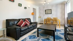 A modern living room with a leather sofa, a dining table with chairs, a TV, and a patterned rug.