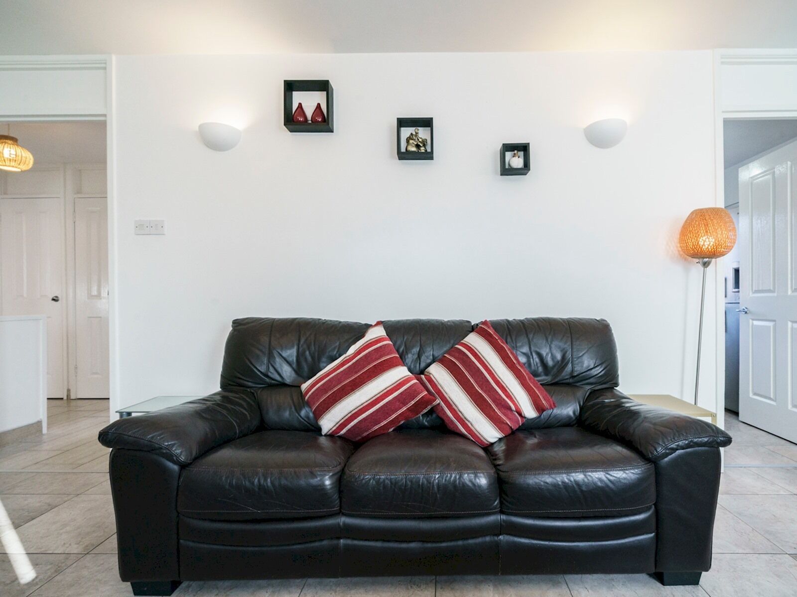 Un canapé en cuir marron foncé agrémenté de deux coussins à rayures, un mur blanc orné de trois tableaux encadrés et un lampadaire.