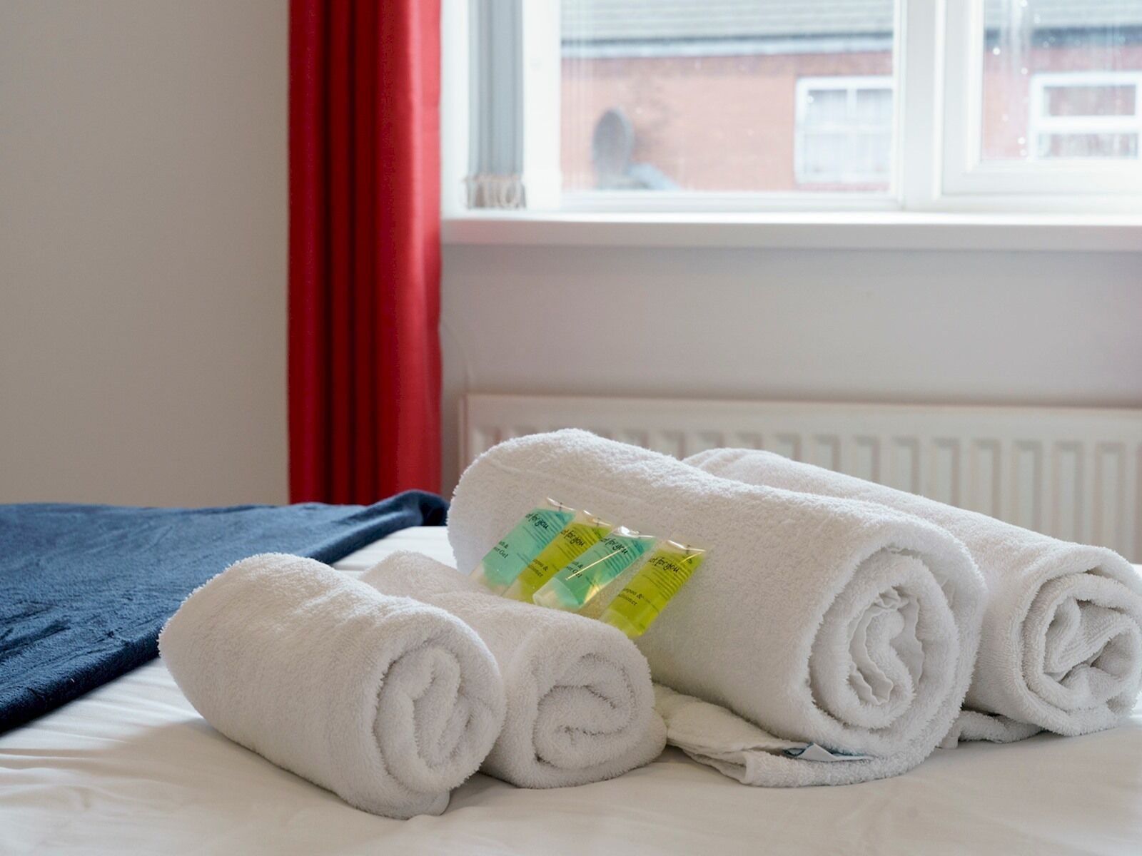 Un lit bien fait, avec des serviettes blanches pliées en rouleaux et une couverture bleue.