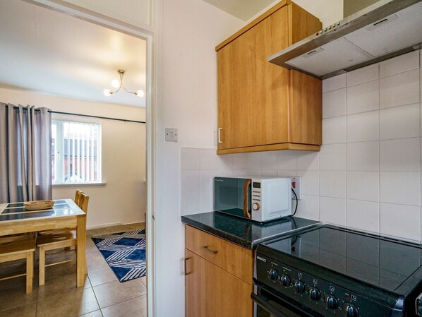 Una cocina compacta con armarios de madera, un microondas, una estufa y un comedor con mesa y sillas.