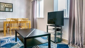 A modern living room with a dining area, a flat-screen TV, and a glass TV stand.