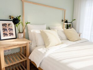 Une chambre à coucher bien rangée, avec une tête de lit en bois, une table de chevet avec une lampe, un tableau encadré et deux plantes en pot.