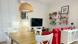 Een moderne woonkamer met een houten eettafel, witte stoelen, een rode bank, een televisie en een boekenkast.
