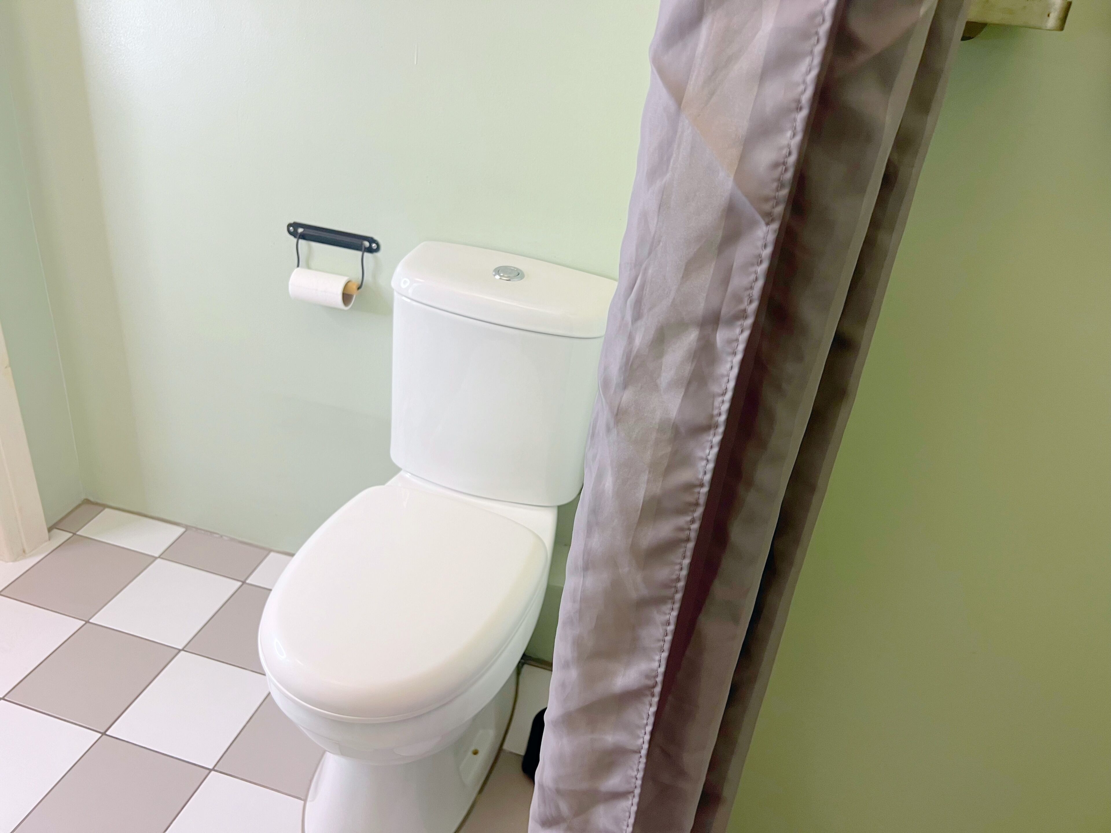 A toilet with a white tank and lid, a toilet paper holder on the wall, and a tiled floor.