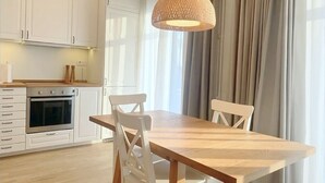 Een moderne keuken met witte kastjes, een houten eettafel en een geweven hanglamp.
