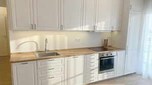 Een keuken met witte kastjes, een gootsteen, een fornuis en een raam met gordijnen.