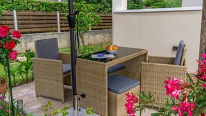 A patio area with wicker furniture, a table with a bowl of fruit, and a metal pole. - Apartment Adria Nr. 2 with garden and grill (Baska)