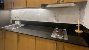 A modern kitchen with wooden cabinets, a black countertop, a stainless steel sink, and a built-in stove. - Stunning Mall of Asia View @ Shell Residences (Pasay)