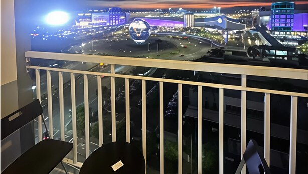 A balcony with a view of a cityscape at night, including a large illuminated globe and various buildings. - Stunning Mall of Asia View @ Shell Residences (Pasay)