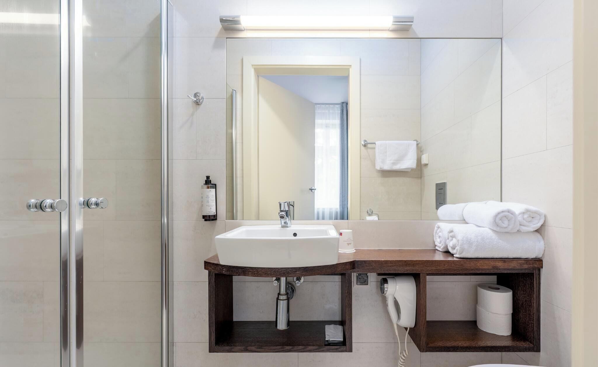 A modern bathroom with a glass shower enclosure, a sink with a wooden vanity, a mirror, and a towel rack.