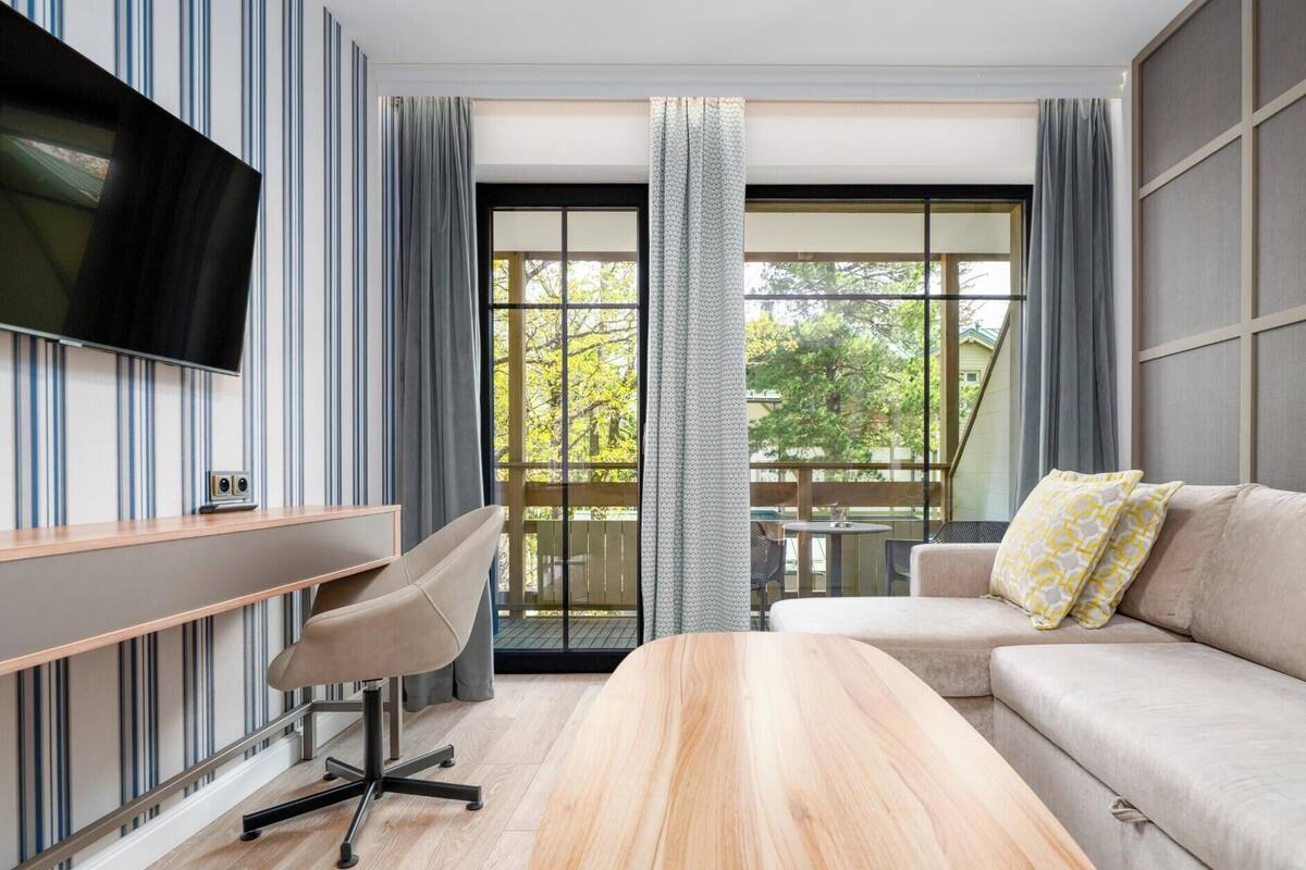 Een moderne hotelkamer met een bank, een bureau, een televisie en een groot raam met gordijnen.