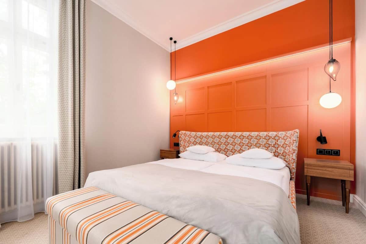 Een slaapkamer met een bed, nachtkastjes, een raam met gordijnen en een muur met een patroon.