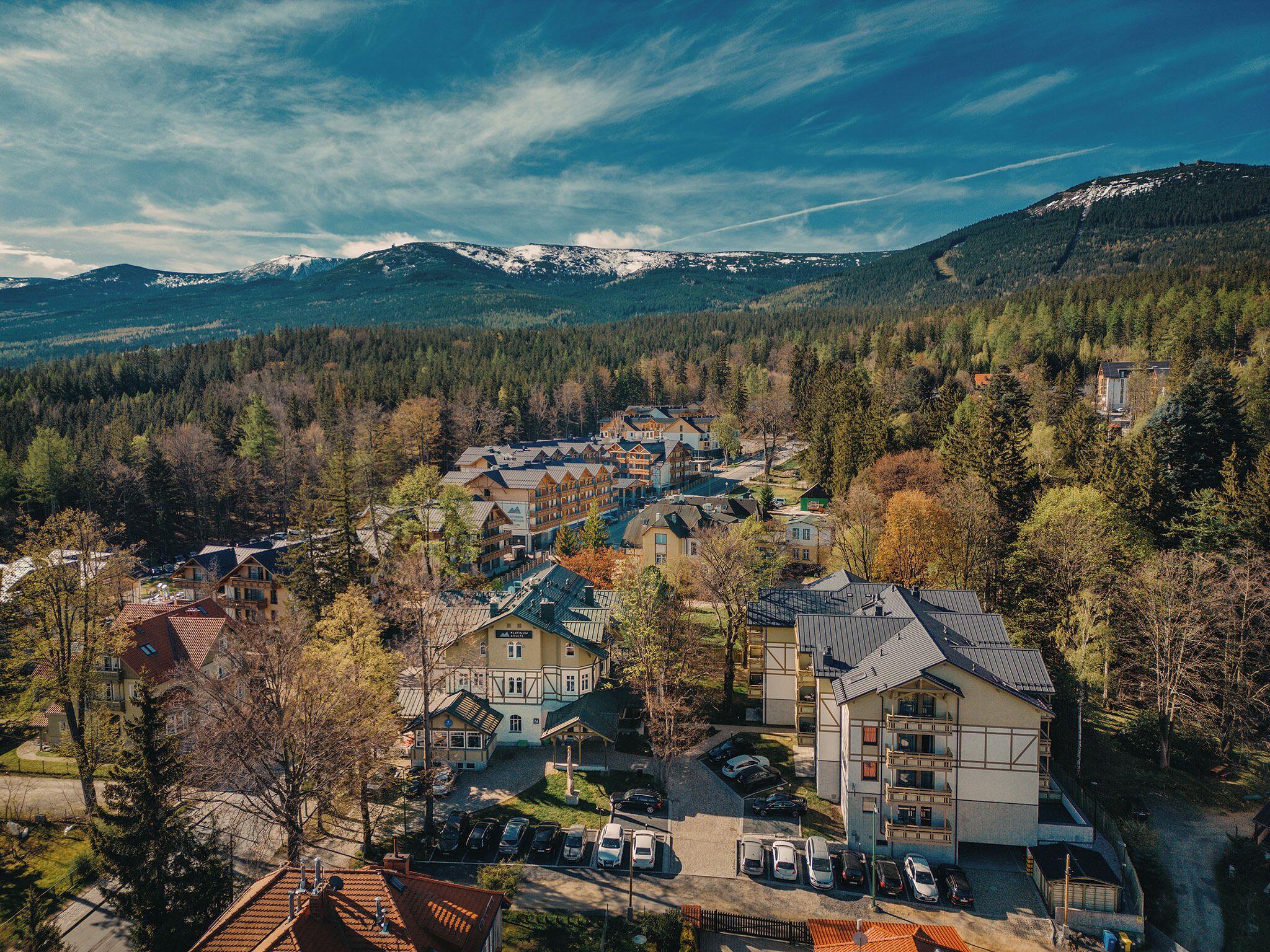 Um resort de montanha com vários edifícios, área de estacionamento e vista para montanhas cobertas de neve.