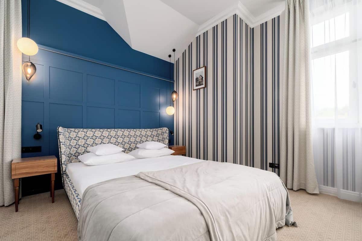 Een slaapkamer met een groot bed, een nachtkastje, een wandlamp en behang met strepen.
