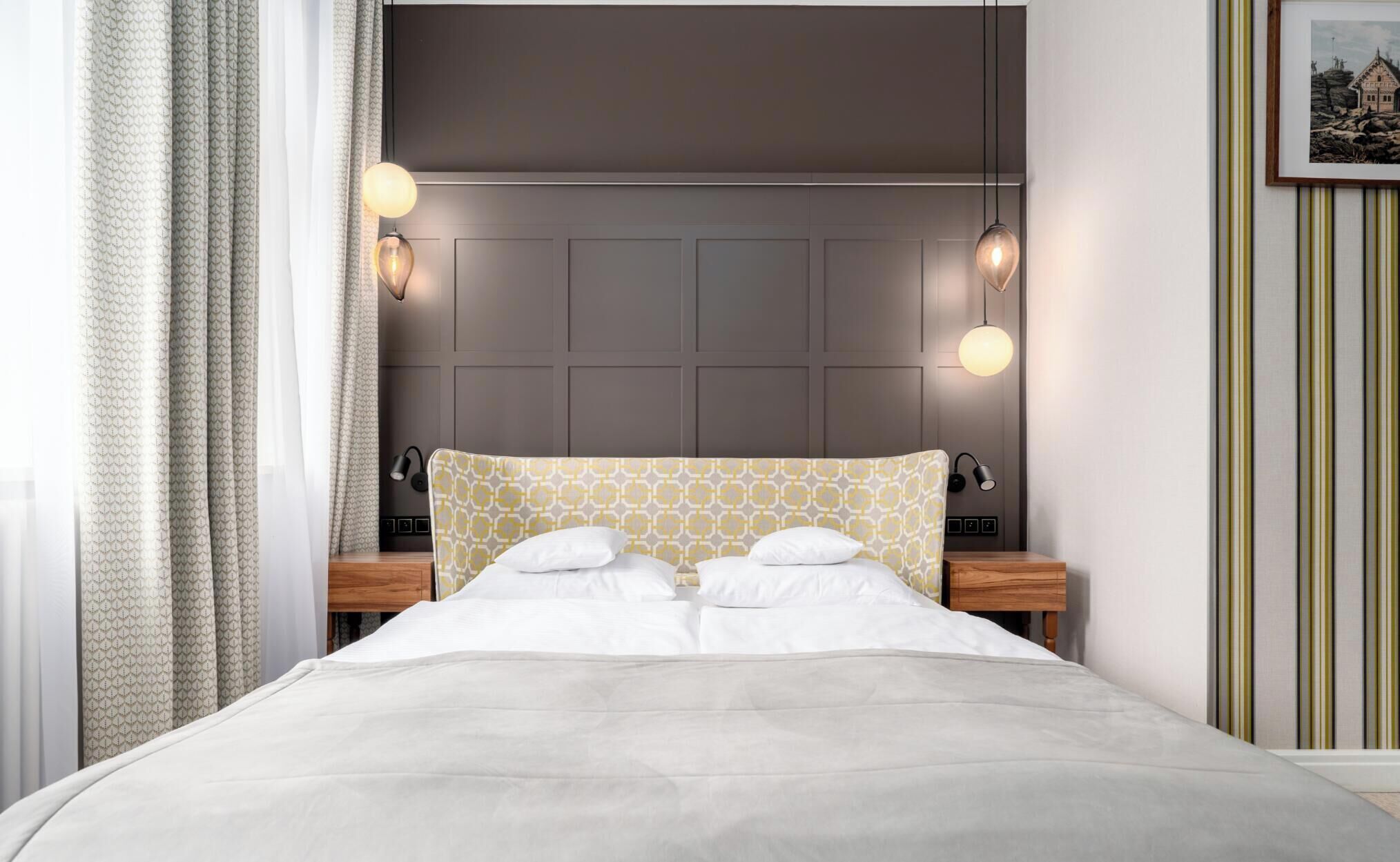 A neatly made bed with a patterned headboard, bedside lamps, and a framed picture on the wall.