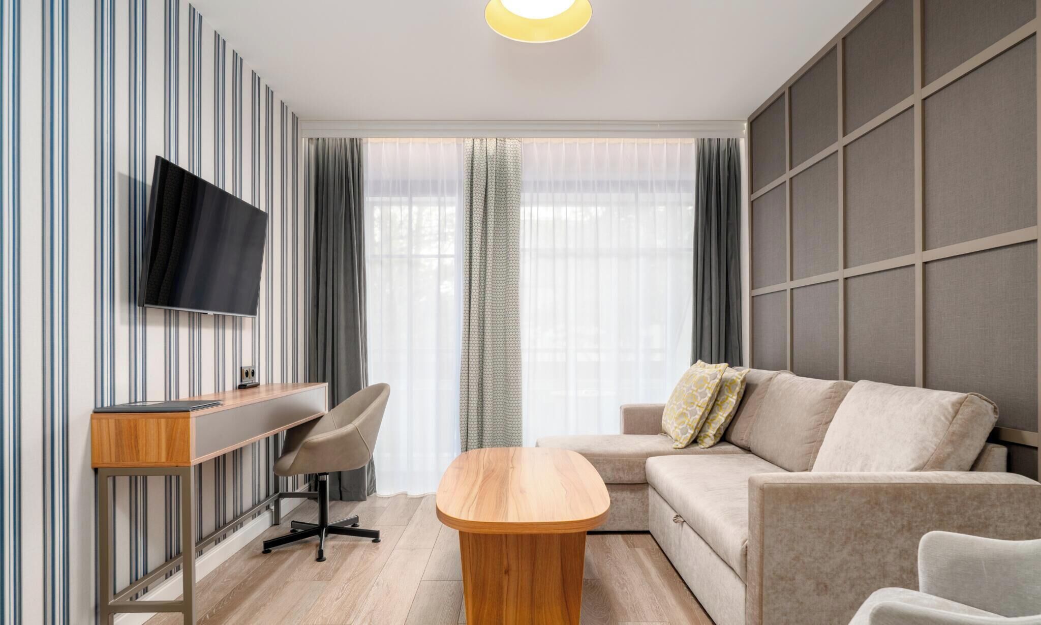A modern living room with a flat-screen TV, a wooden coffee table, a sofa, and a desk with a chair.