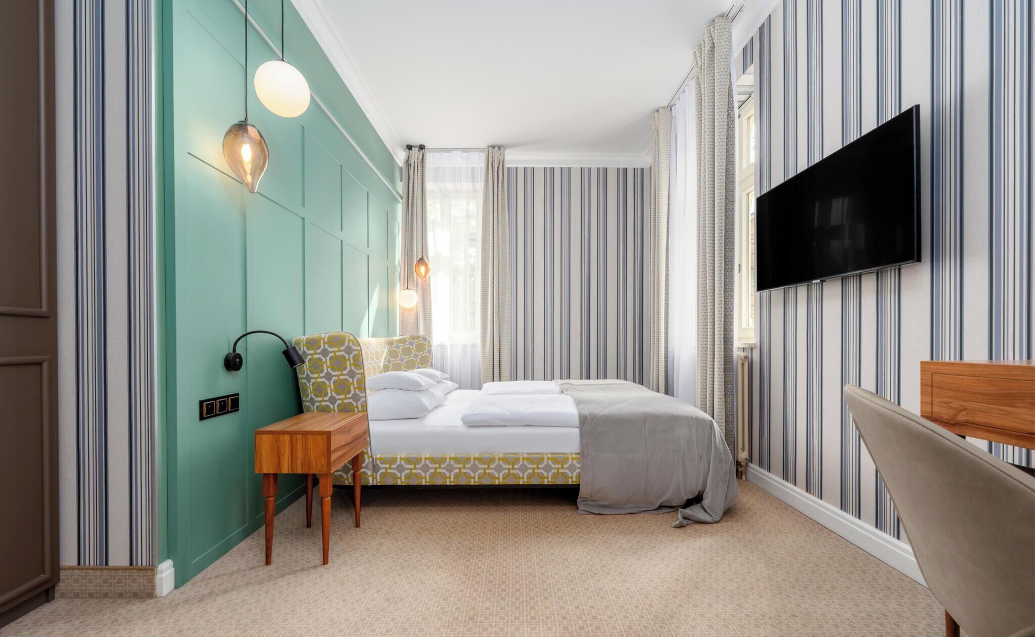 Ein Hotelzimmer mit Bett, Nachttisch, Lampe, Fernseher und gestreifter Tapete.
