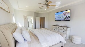 A bedroom with a large bed, a ceiling fan, a dresser, and a TV on the wall.