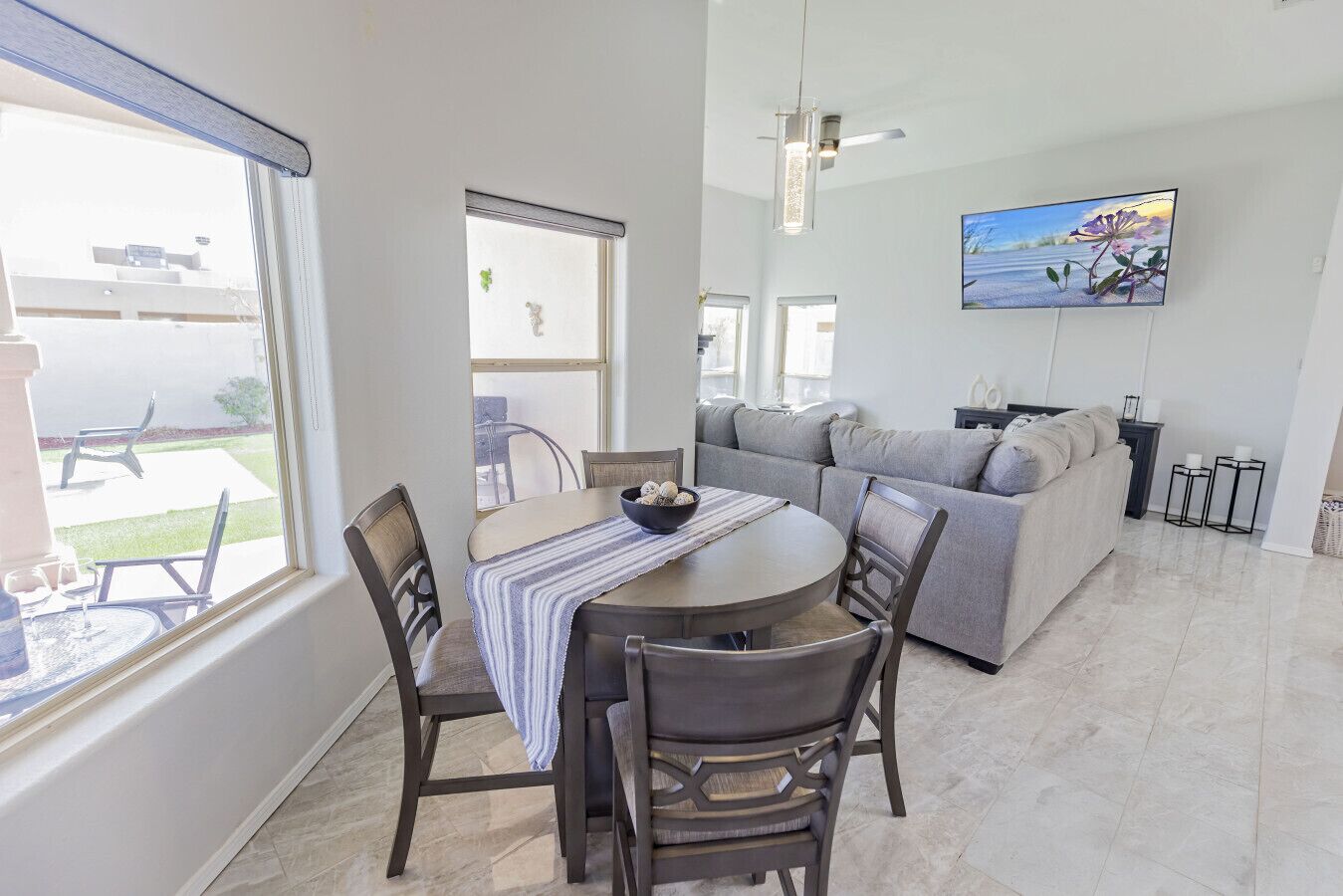 A dining area with a round table, chairs, and a bowl. There is a sofa and a TV mounted on the wall.