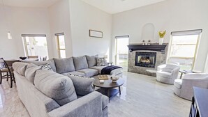 A spacious living room with a large grey sectional sofa, a round coffee table, and a fireplace.