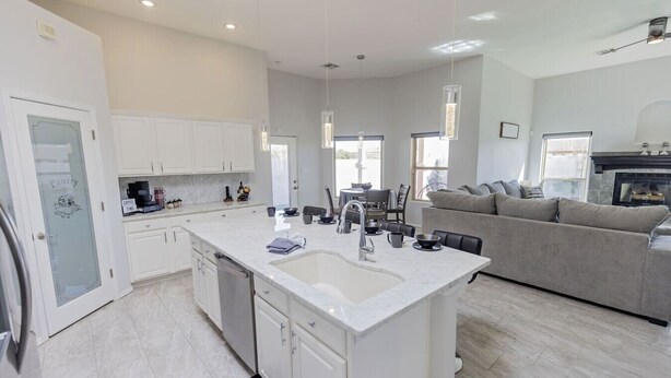 A modern kitchen with a large island, white cabinetry, and a dining area with a grey sofa.