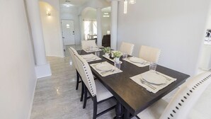 A dining area with a long table set for four, white chairs, and modern pendant lighting.
