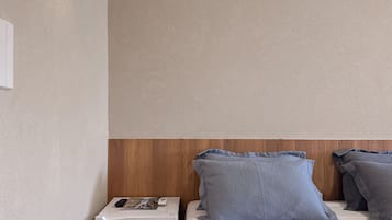 Una habitación de hotel con cama, un calentador pequeño, una mesita de noche y una lámpara fijada en la pared.