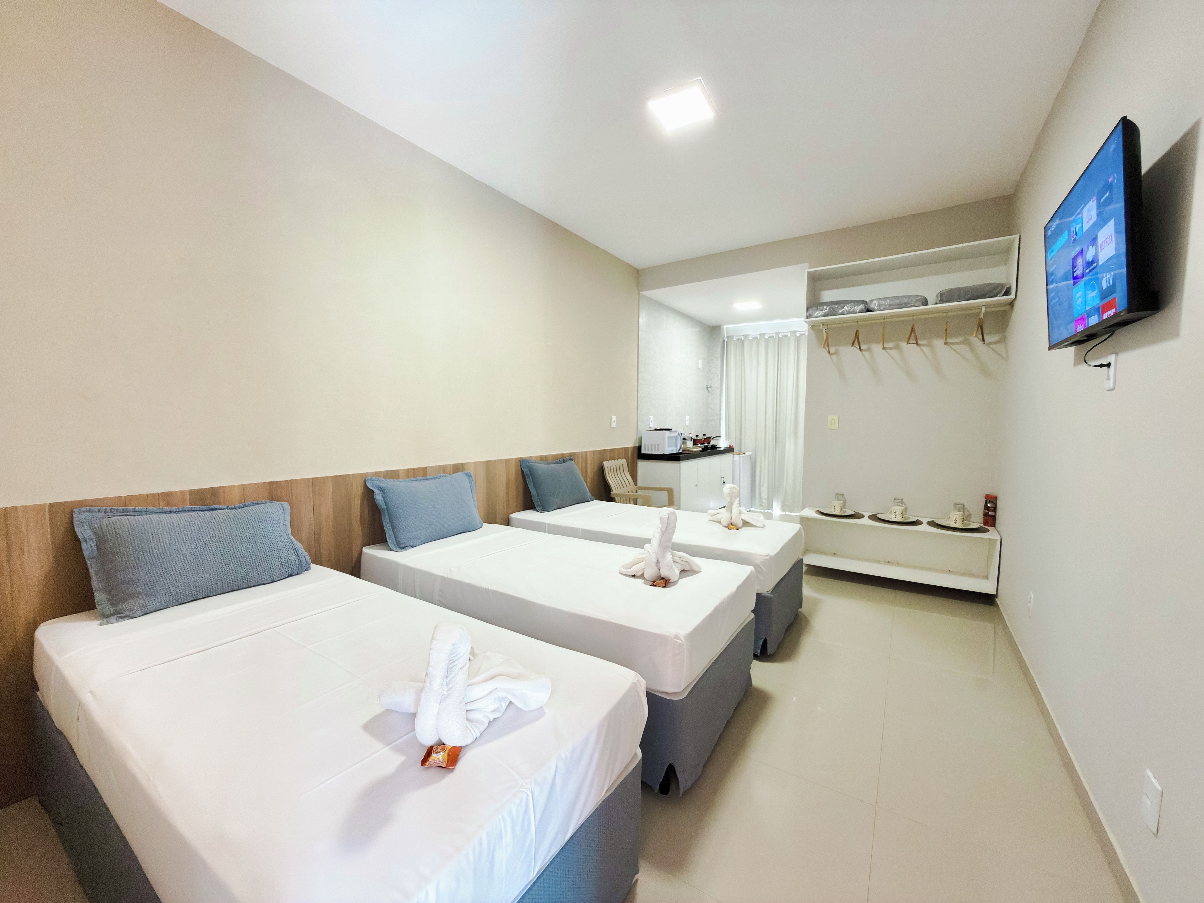 Quarto de hotel com duas camas, televisão, guarda-roupa e cozinha compacta.