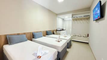 Quarto de hotel com duas camas, televisão, guarda-roupa e cozinha compacta.