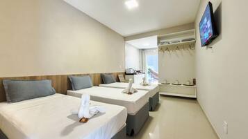 Quarto de hotel com duas camas, uma televisão fixada na parede e vista para o mar pela janela.