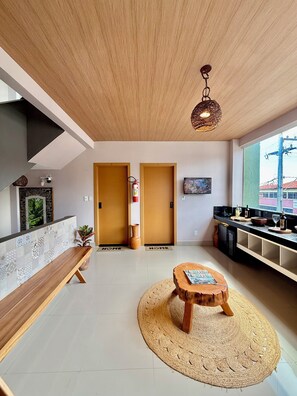Een moderne woonkamer met een houten bankje, een ronde salontafel en een groot raam met uitzicht op gebouwen.