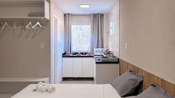A hotel room with two beds, a kitchenette, a bathroom, and a view of the outside.